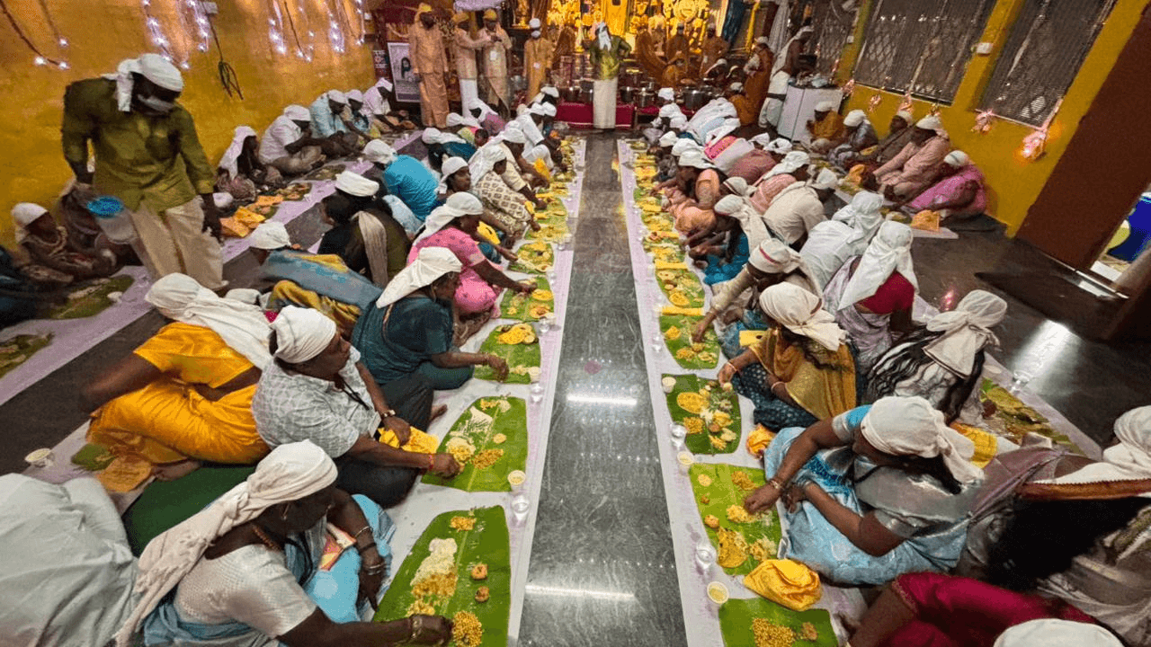 Devotees seated in long rows on the floor, served a meal on banana leaves at the annadhanam